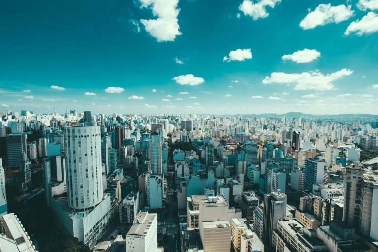 Sunny aerial view of São Paulo skyline with dense high-rise buildings under blue skies.