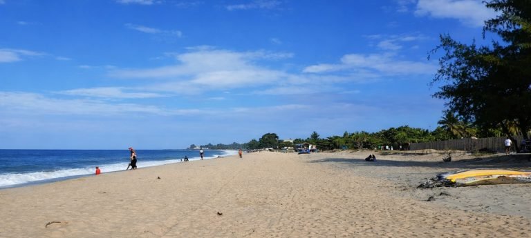 Wide sandy beach in Tamatave (Toamasina), Madagascar, with gentle waves, a few walkers, and a bright blue sky.