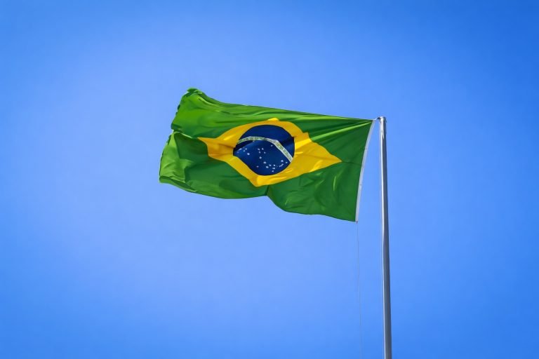 Brazilian flag waving on a flagpole against a clear, bright blue sky on a sunny day.