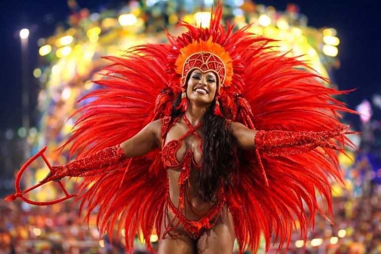 Brazil Carnival samba dancer in bright red feathered costume performing under colorful festival lights.