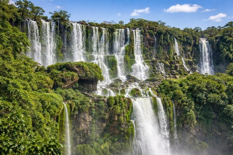 Iguazu Falls Brazil cascading over lush green cliffs under blue skies on a sunny afternoon in Brazil