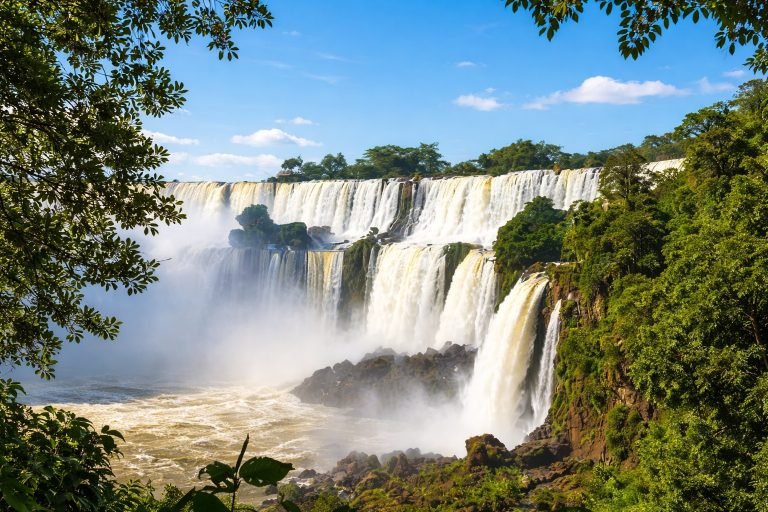Iguazu Falls Brazil on a sunny afternoon with blue skies and vibrant rainforest surrounding the powerful cascading waterfalls