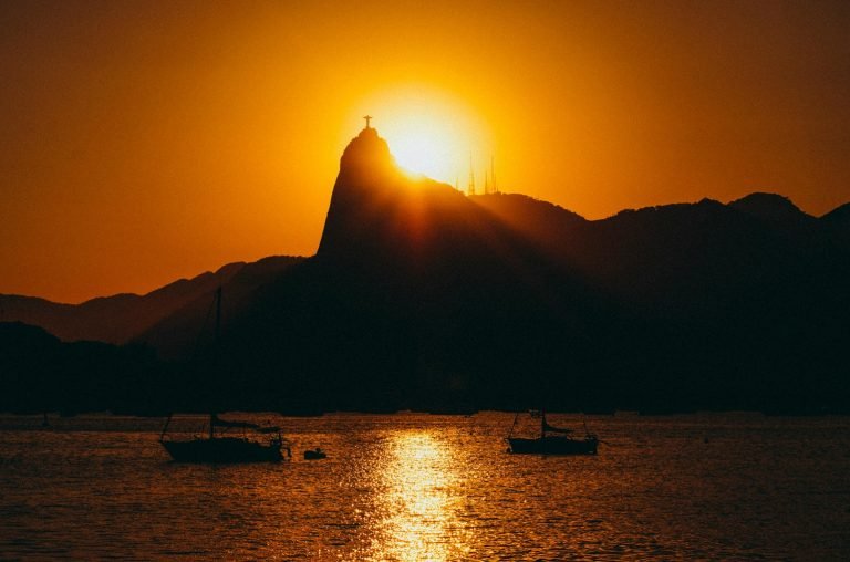 Christ the Redeemer silhouette at sunset over Rio de Janeiro with golden reflection on Guanabara Bay