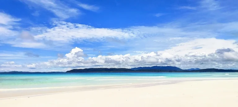 Plage de sable blanc et lagon turquoise sous un ciel bleu à Madagascar