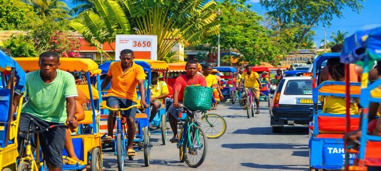 Pousse-pousse colorés et cyclistes dans une rue animée de Madagascar
