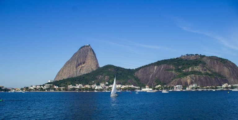Sugarloaf Mountain Rio de Janeiro seen across Guanabara Bay with sailboat in foreground and Urca neighborhood below