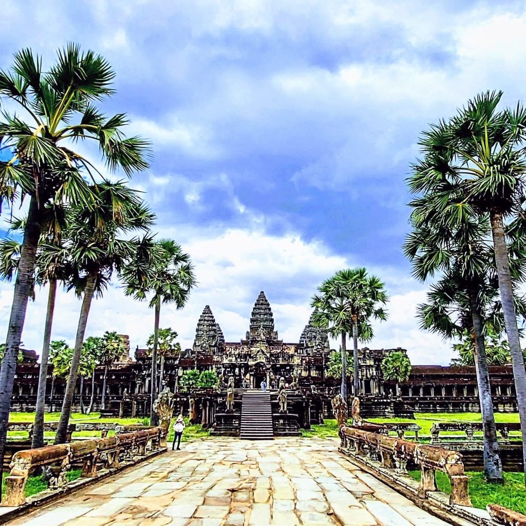 Things to do in Cambodia: Angkor Wat temple complex in Siem Reap with palm trees and stone walkway under a dramatic sky