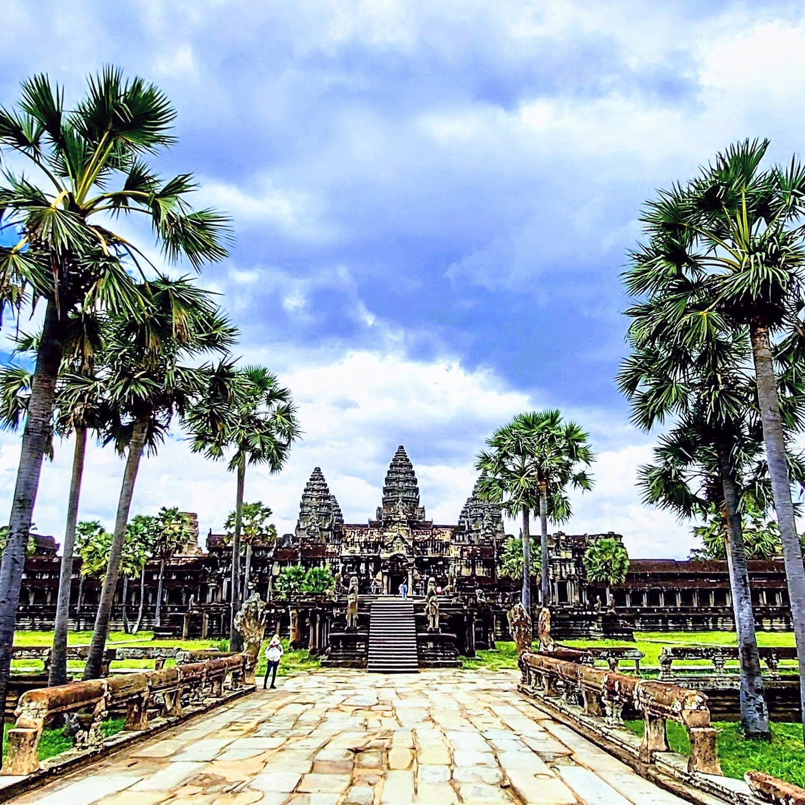 Things to do in Cambodia: Angkor Wat temple complex in Siem Reap with palm trees and stone walkway under a dramatic sky