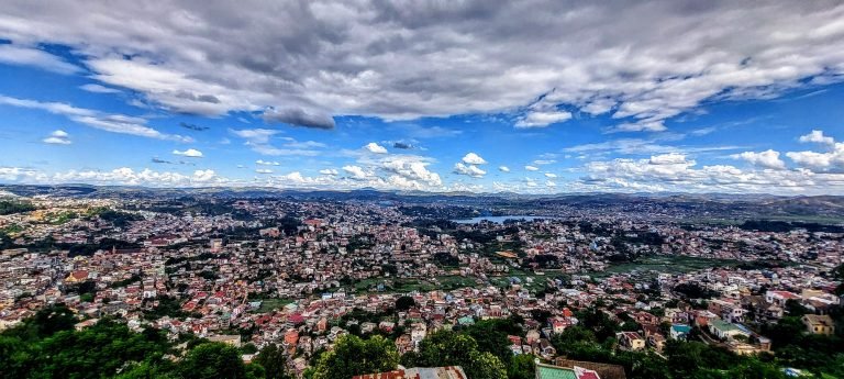 Madagascar Travel Cost - Panoramic view of Antananarivo Madagascar with hills, houses, and Lake Anosy under a cloudy blue sky