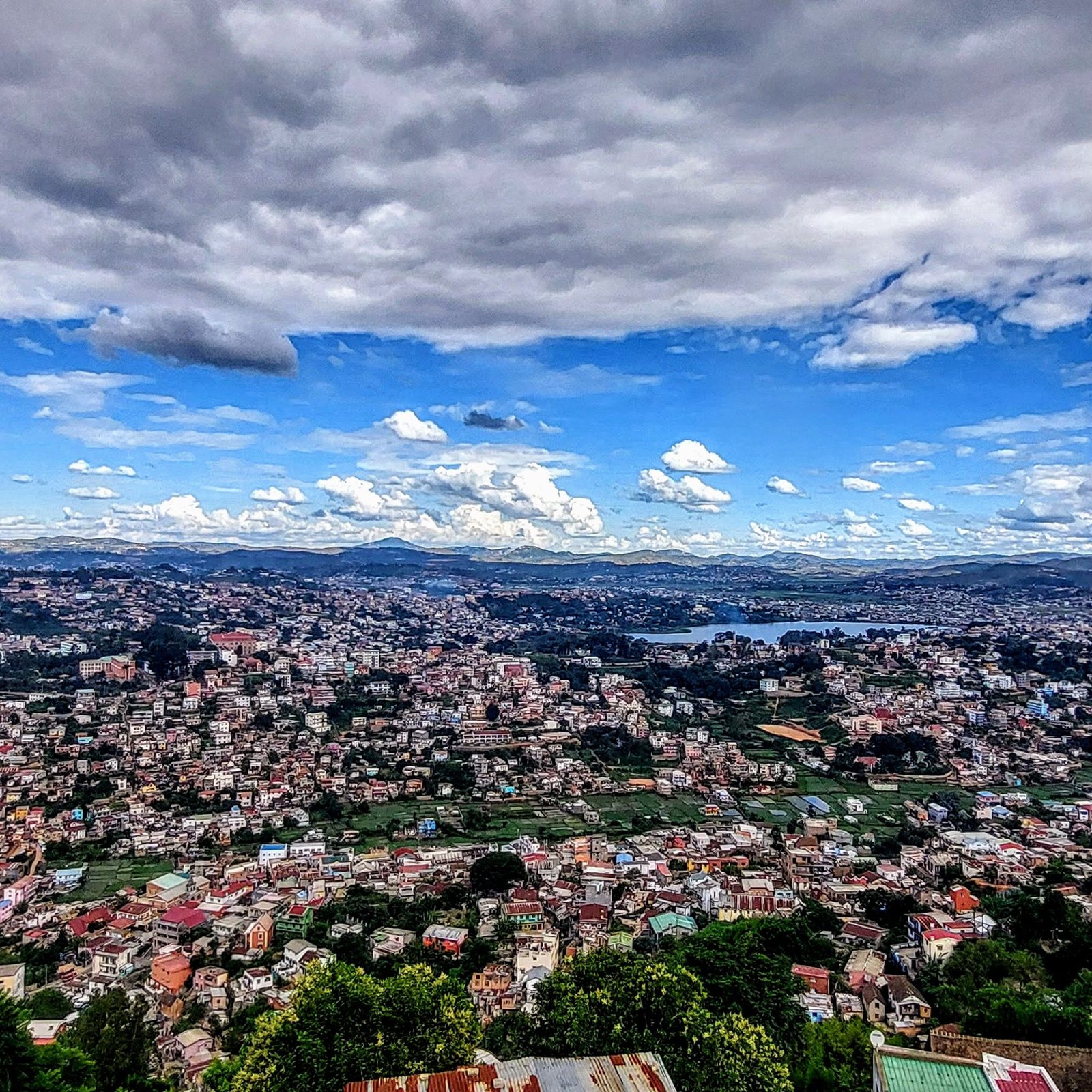 Madagascar Travel Cost - Panoramic view of Antananarivo Madagascar with hills, houses, and Lake Anosy under a cloudy blue sky