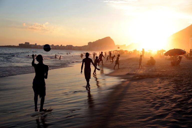 Is Rio safe - Beach scene in Rio de Janeiro at sunset with people walking along the shoreline