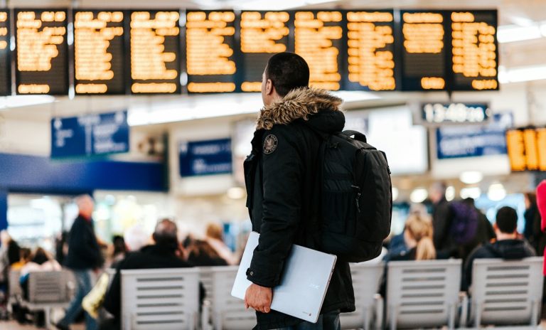 Traveler at airport departure board comparing credit-card-travel-insurance-vs-travel-insurance before international trip