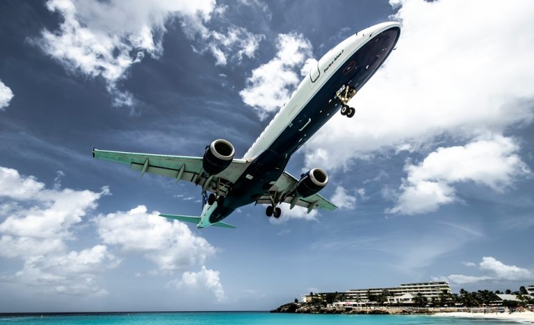 Airplane landing over tropical beach illustrating credit-card-travel-insurance-vs-travel-insurance for flight disruptions
