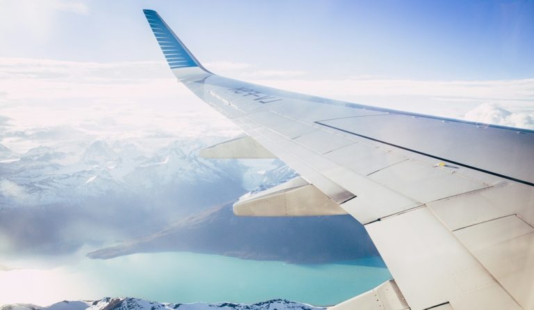Airplane wing view over mountains illustrating credit-card-travel-insurance-vs-travel-insurance for international flights Caption: Description: