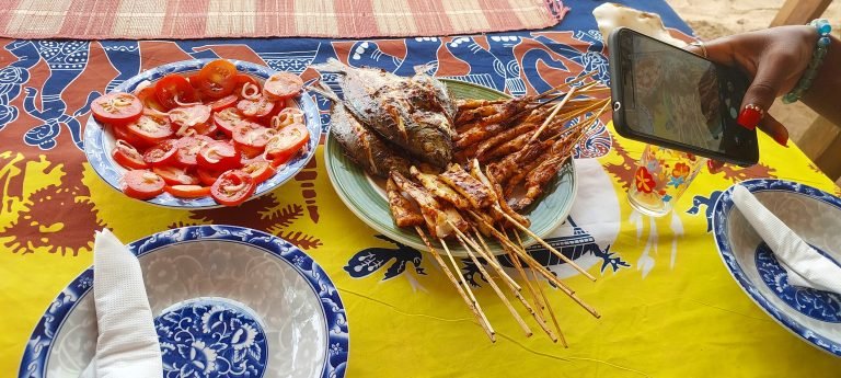 Madagascar food - street scene with grilled seafood skewers, whole fish and fresh tomato salad served on a colorful table