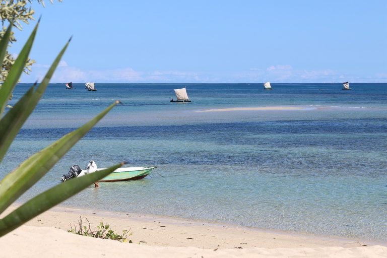 Madagascar beach with traditional sailboats on turquoise water and white sand shoreline Caption: Description: