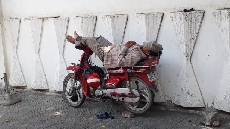 Things to do in Cambodia: local man sleeping on a motorcycle parked on a Phnom Penh street