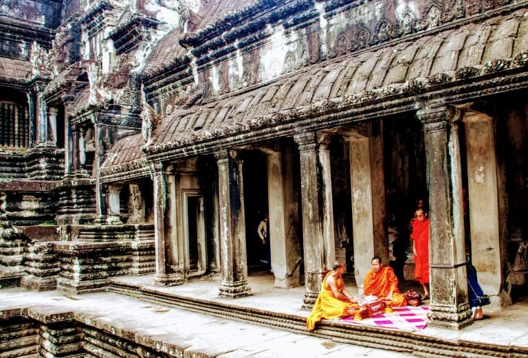 Things to do in Cambodia: Buddhist monks sitting inside Angkor Wat temple in Siem Reap with ancient stone carvings 📝 Caption 📖 Description
