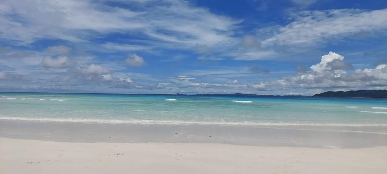 Tropical beach in Madagascar with turquoise water, white sand, and bright blue skies Caption Description
