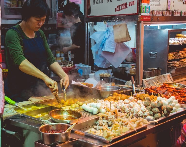 Raohe night market street food vendor cooking skewers, fish balls, and Taiwanese snacks at a busy Taipei night market stall