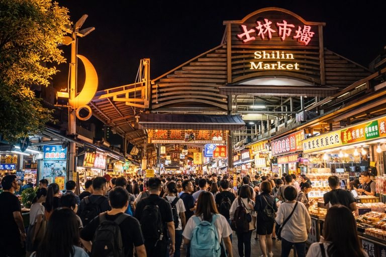 Entrance of Shilin Taiwan Night Market in Taipei at night with bright neon sign, busy food stalls, and large evening crowds exploring the market.