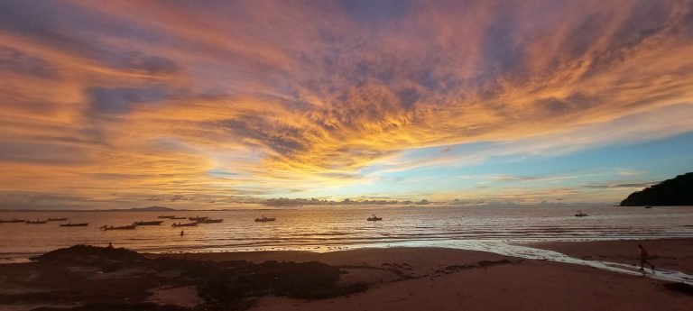 Sunset over the ocean on a Madagascar beach with fishing boats on the horizon