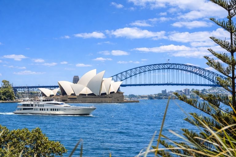 Sydney Harbour Cruises - Yacht passing Sydney Opera House and Harbour Bridge on a bright sunny day with blue skies