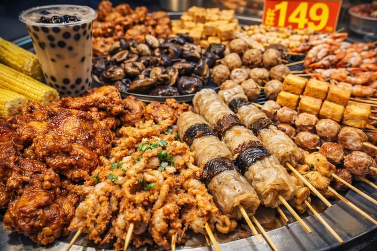 Fengjia Night Market street food specialties including skewers, grilled meats, fried snacks, and bubble tea displayed at a food stall in Taichung Taiwan