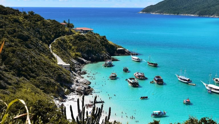 Aerial view of Arraial do Cabo beach with turquoise water, boats, and swimmers along the coastline
