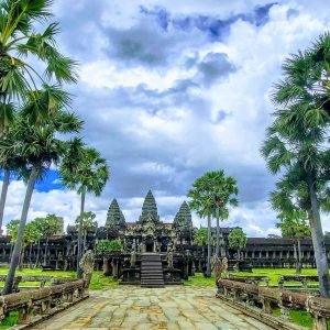 Angkor Wat Guide - View of the temple entrance with palm trees and dramatic sky in Siem Reap Cambodia
