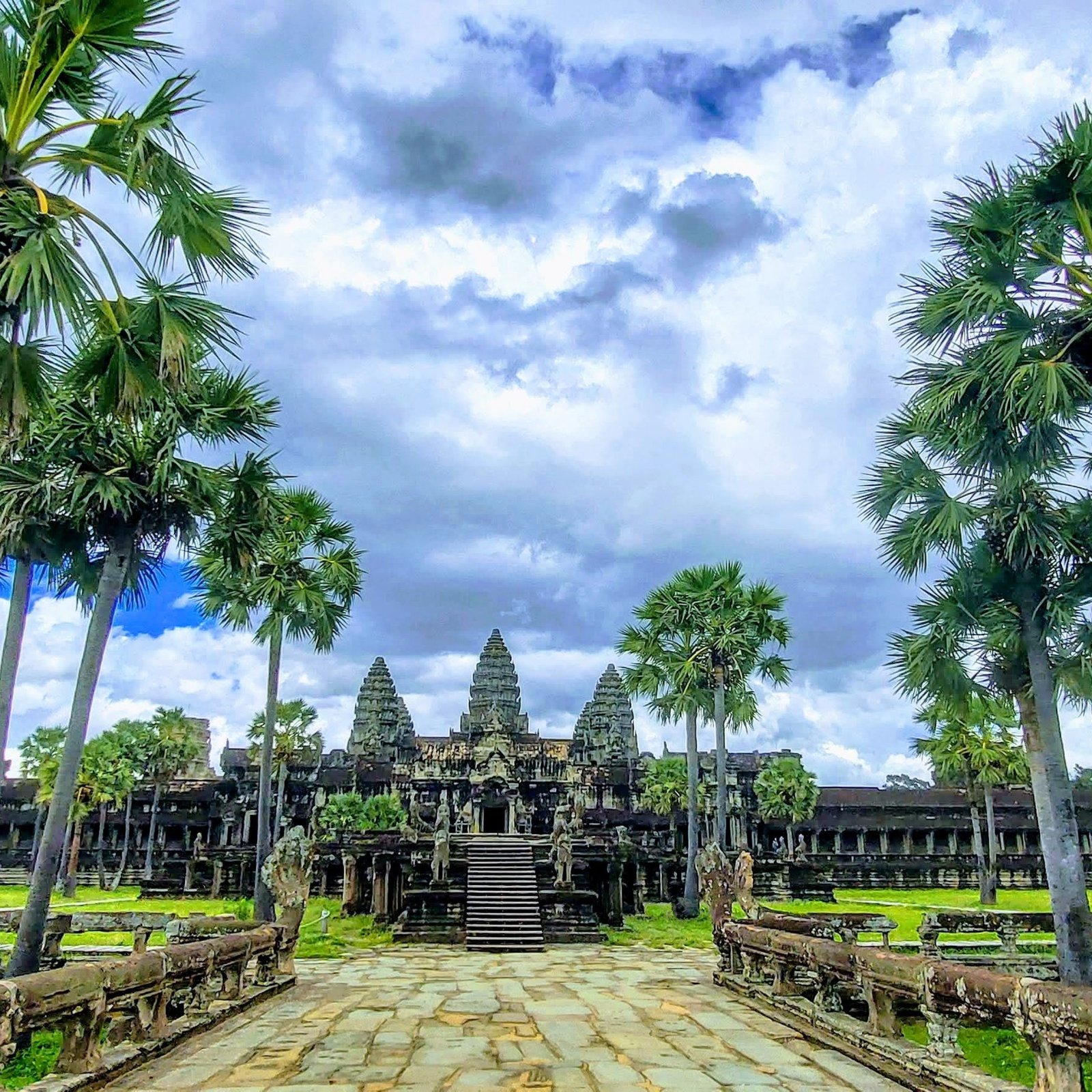 Angkor Wat Guide - View of the temple entrance with palm trees and dramatic sky in Siem Reap Cambodia