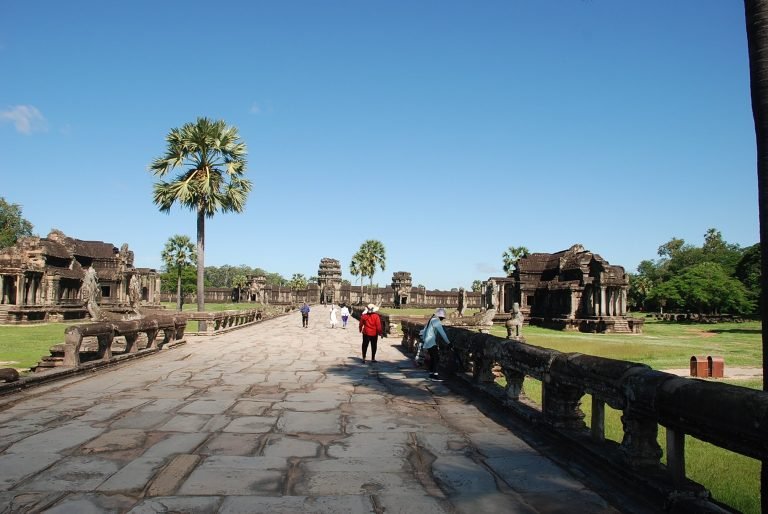 Angkor Wat Guide showing visitors walking along the main stone causeway toward the temple entrance in Siem Reap Cambodia Caption Description