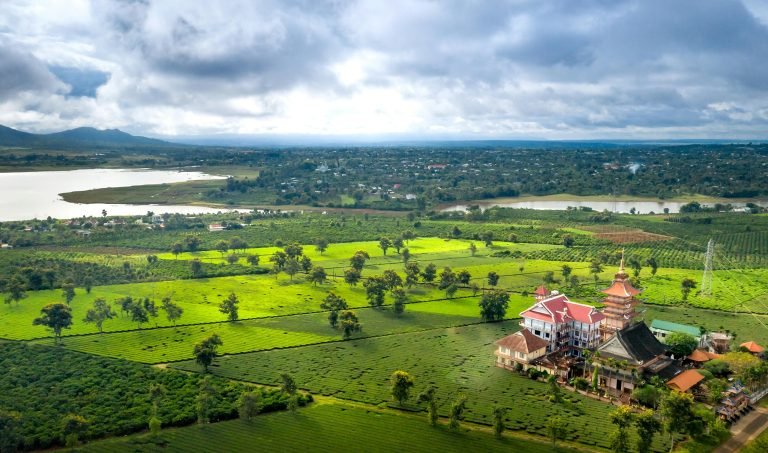Aerial view of Battambang countryside with green rice fields, river, and temple complex in Cambodia Caption: Description: