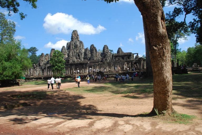 Angkor Wat Guide showing Bayon temple with stone face towers and visitors in Angkor Thom Siem Reap Cambodia Caption Description