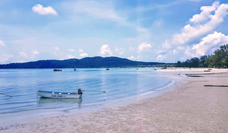 Beach on Koh Rong Samloem with calm shallow water, small boat, and wide sandy shoreline
