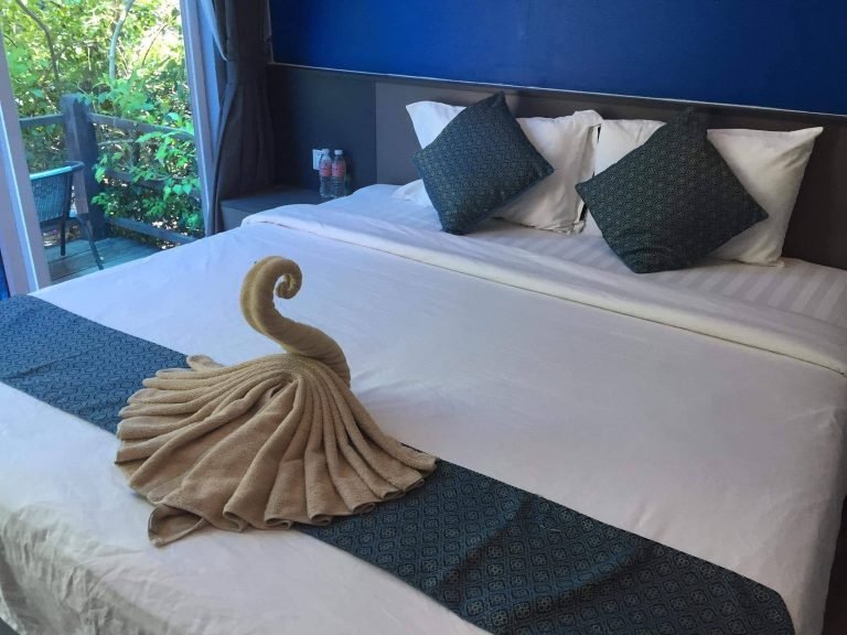 Cambodia itinerary hotel room with comfortable bed, towel decoration, and balcony view in a tropical setting Caption Description