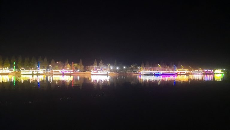 things to do in Kampot illuminated river boats at night with colorful reflections on water Caption Description