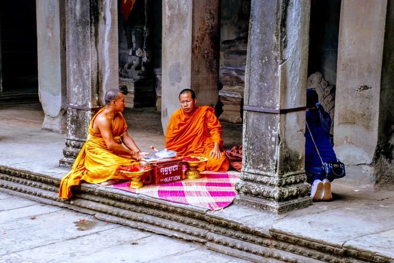 Buddhist monks in orange robes receiving donation and blessing visitor inside Angkor Wat temple Cambodia