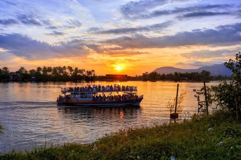 Things to do in Kampot - Sunset river cruise boat with people and mountain backdrop