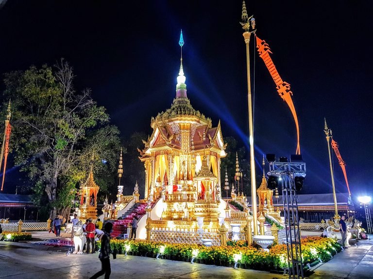 Brightly lit Cambodian temple at night with golden architecture, traditional decorations, and people attending a ceremony