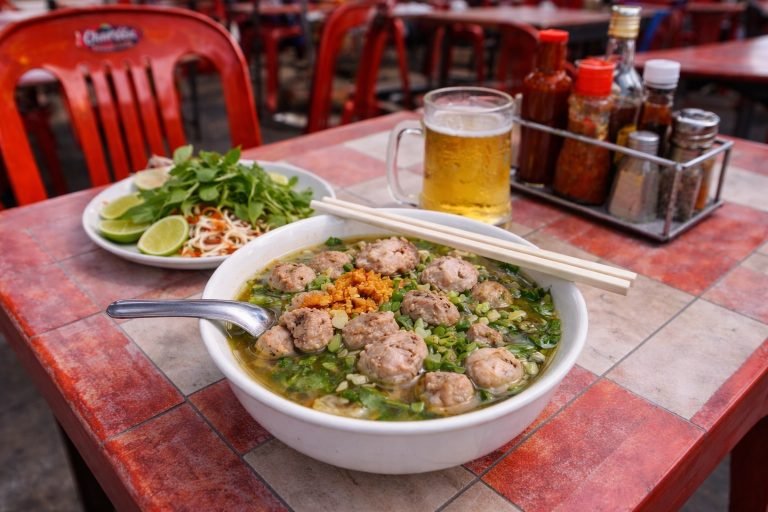 Cambodian food kuy teav noodle soup served on a street food table with red plastic chairs and local condiments Caption Description