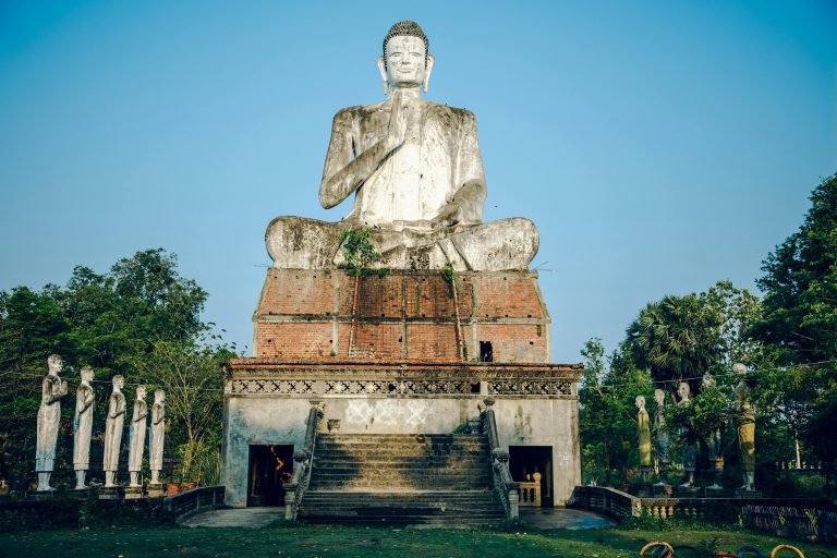 Large seated Buddha statue at Phnom Sampeau in Battambang Cambodia surrounded by trees and temple structures
