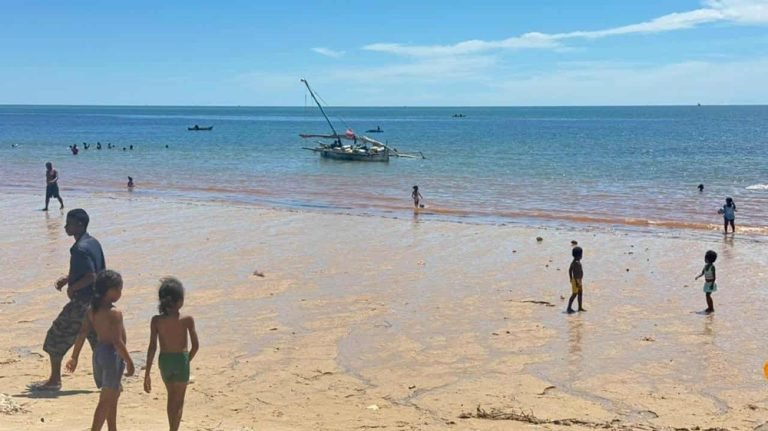 children and families on a beach in Madagascar with fishing boat offshore