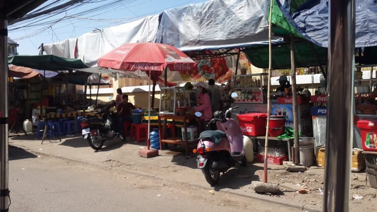 Street food stall in Cambodia with motorbikes parked and locals preparing fresh meals