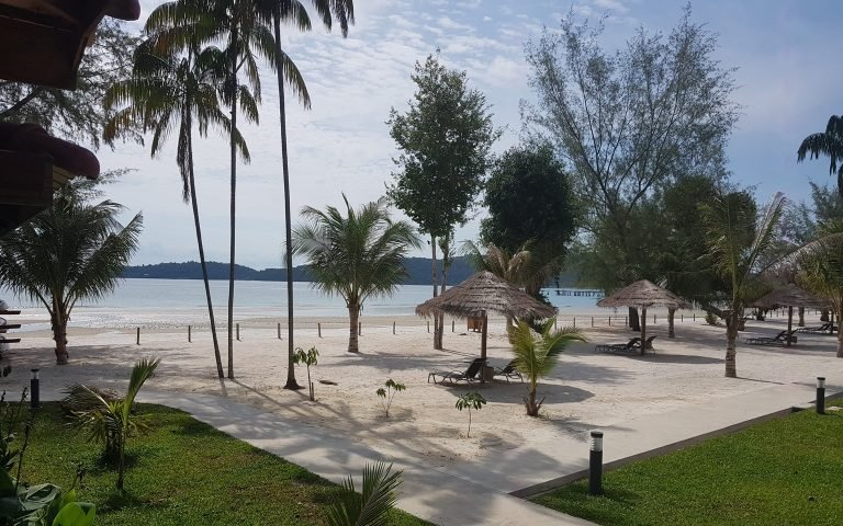 Beach seating area on Koh Rong Samloem with palm trees, thatched umbrellas, and white sand near the shoreline
