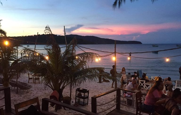 Beachfront restaurant on Koh Rong samloem at sunset with lights, tables on the sand, and calm sea views
