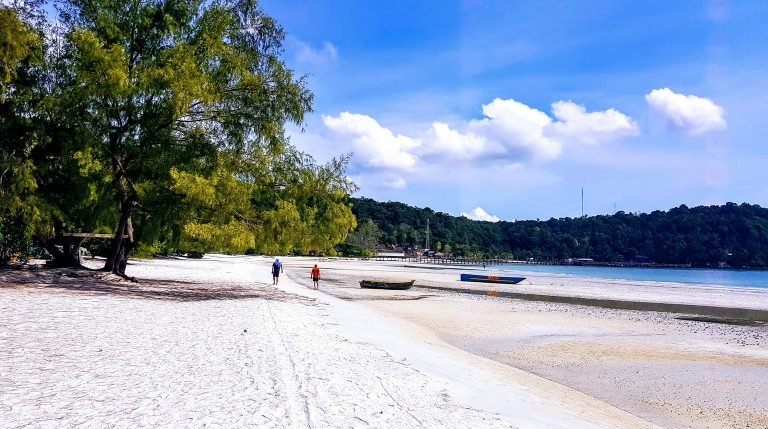 Koh Rong samloem beach with white sand, shallow water, and people walking along the tropical coastline Caption: Description: