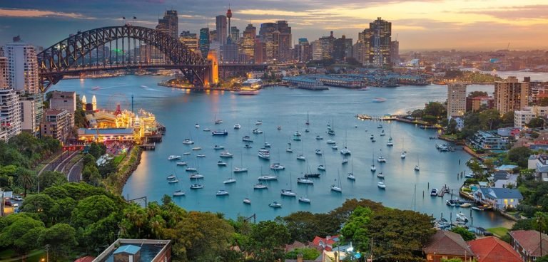Sydney travel tips: aerial view of Sydney Harbour Bridge, skyline, and boats at sunset
