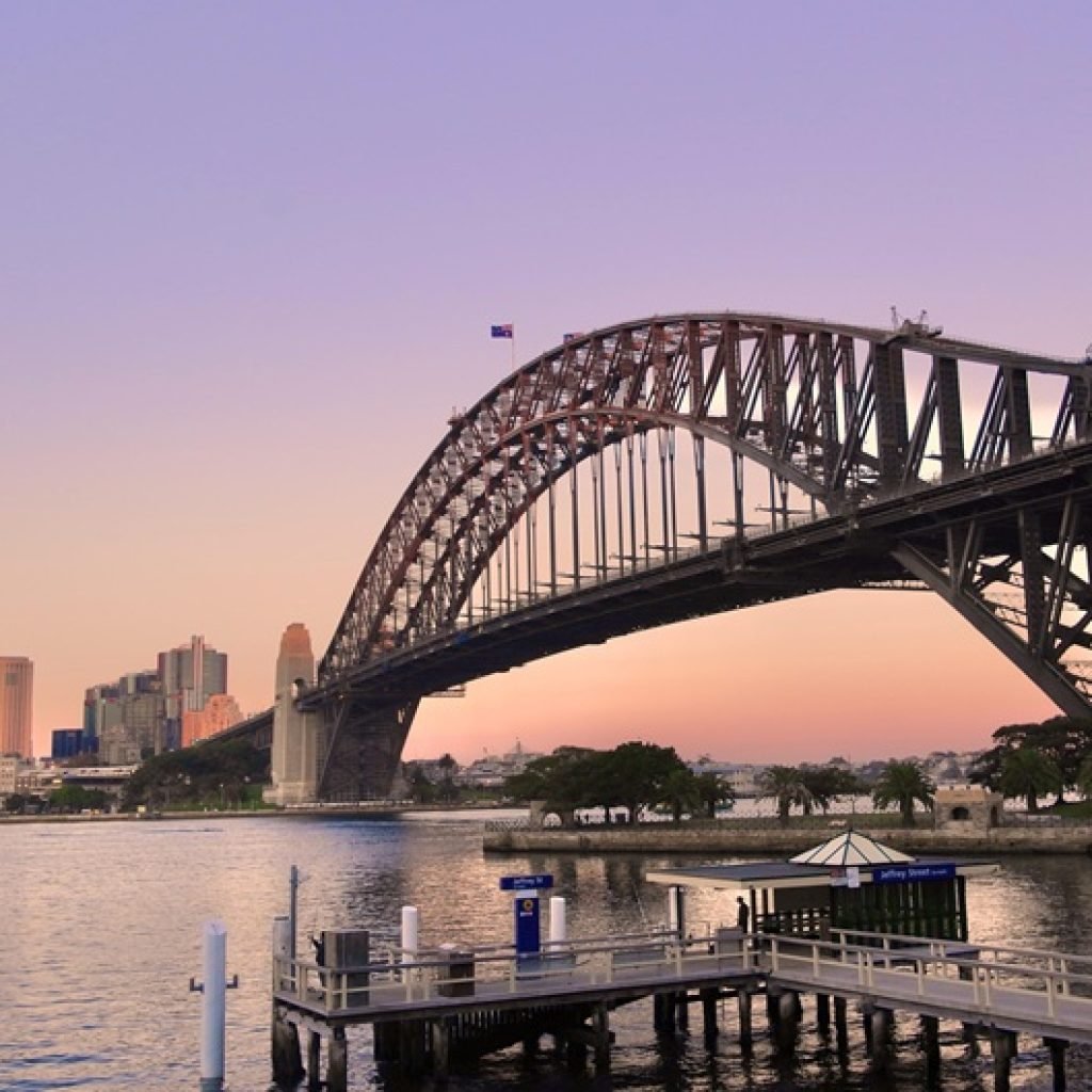 Sydney travel tips: view of the Sydney Harbour Bridge at sunset with skyline and ferry pier