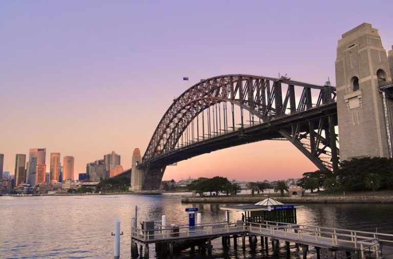 Sydney travel tips: view of the Sydney Harbour Bridge at sunset with skyline and ferry pier